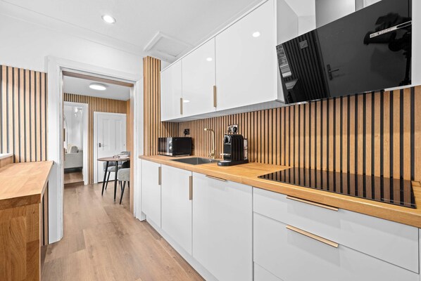 Una cocina moderna con armarios blancos, encimera de madera y microondas negro.