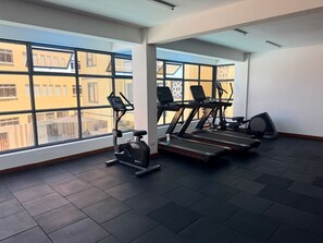 A gym with treadmills, an elliptical, and a stationary bike, large windows, and a tiled floor. - Cozy 1br in Mombasa 3minutes walk to the beach with a fitness room (Mombasa)