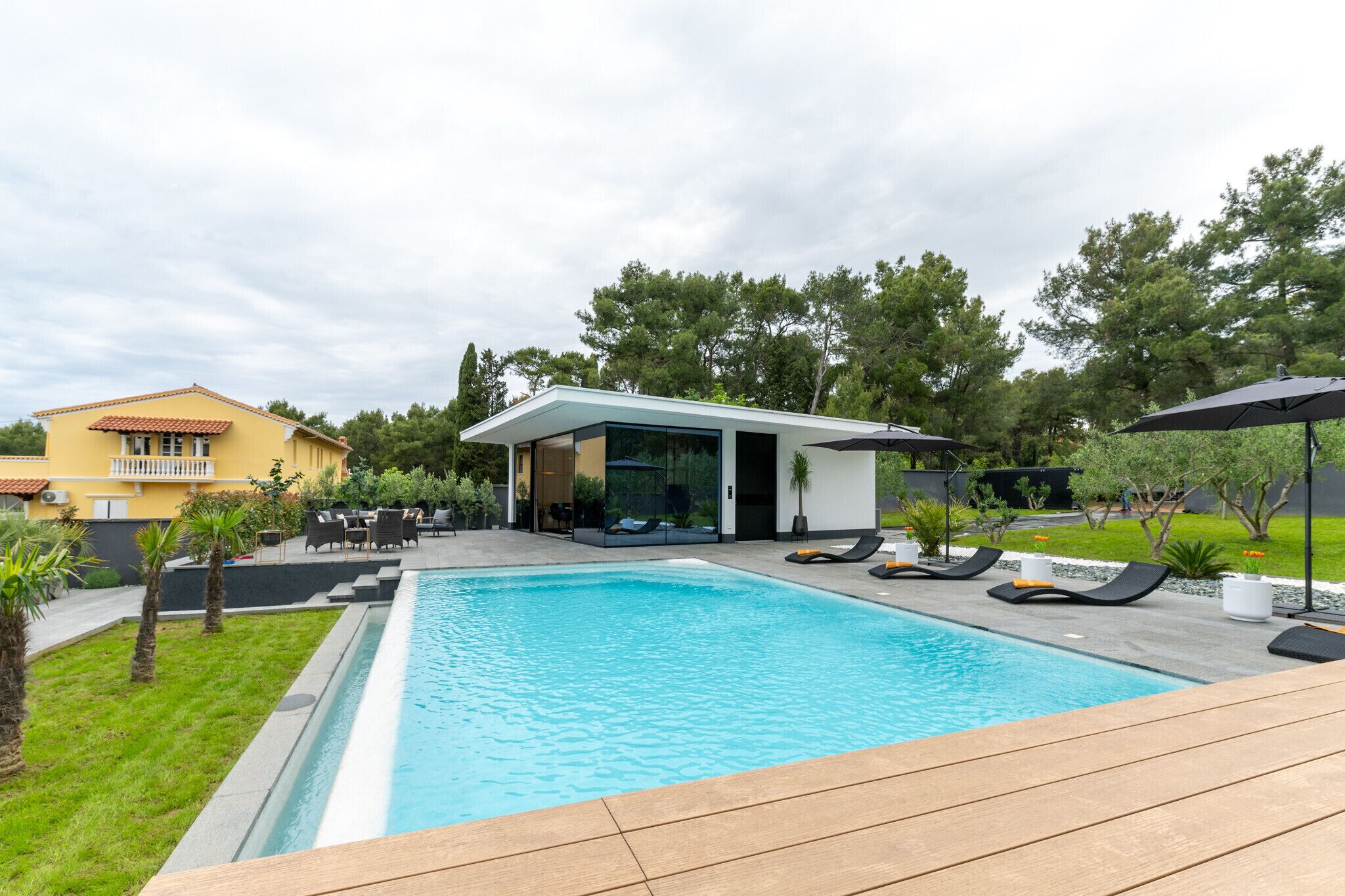 A swimming pool with lounge chairs, a modern house, and a grassy area.