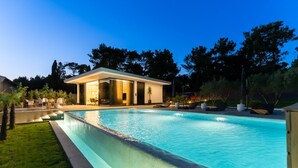 A modern outdoor pool area with a glass-enclosed structure, surrounded by well-maintained grass and trees. - Luxury Matos Estate with heated pool (Zadar)