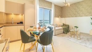 A modern kitchen with a dining area, a sofa, and a small table with a plant. - Manzil - 1BR in Sobha with City Views (Dubai)