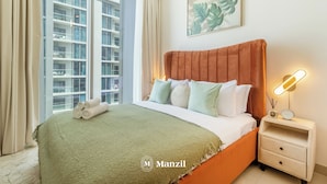 A modern hotel room with a large bed, a nightstand with a lamp, and a view of a high-rise building. - Manzil - 1BR in Sobha with City Views (Dubai)