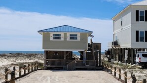 Una proprietà sulla spiaggia con una terrazza in legno, una struttura dal tetto blu e un edificio bianco.