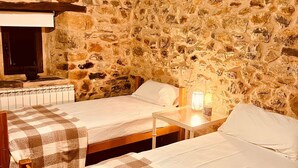 Una habitación con dos camas de madera, una pared de piedra, un televisor y una mesita con una lámpara.