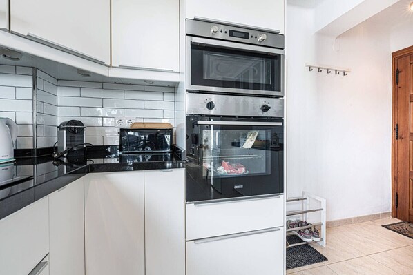 Une cuisine moderne avec des meubles blancs, un plan de travail noir et deux fours.