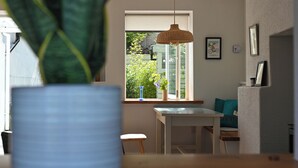 Una planta en maceta sobre una mesa, un comedor con ventana y una lámpara colgante.