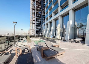 A rooftop pool area with lounge chairs and umbrellas, surrounded by modern buildings and a clear sky. - Stayshort - Chic 1 Bed Bedroom in JVT That Sleeps 2 With Balcony (Dubai)