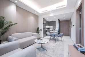 A modern living room with a grey sofa, a round coffee table, and a dining area with chairs. - Stayshort - Chic 1 Bed Bedroom in JVT That Sleeps 2 With Balcony (Dubai)