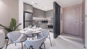 A modern kitchen with a dining area, including a table set for four, chairs, and a refrigerator. - Stayshort - Stunning 1 Bed Bedroom in JVT That Sleeps 2 (Dubai)
