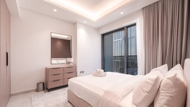A modern bedroom with a large bed, a dresser, a mirror, and a window with curtains. - Stayshort - Stunning 1 Bed Bedroom in JVT That Sleeps 2 (Dubai)