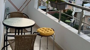 Een balkon met een tafel en stoelen, een bloempot en uitzicht op een stadsbeeld bij zonsondergang.