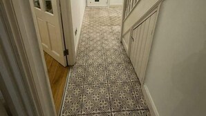 Un couloir doté d’un revêtement de sol à motifs, une porte blanche et un escalier avec une rampe en bois.
