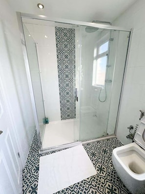 A modern bathroom with a glass-enclosed shower, patterned floor tiles, and a bidet. - Central London in 30 Mins Oxford Street (Ilford)