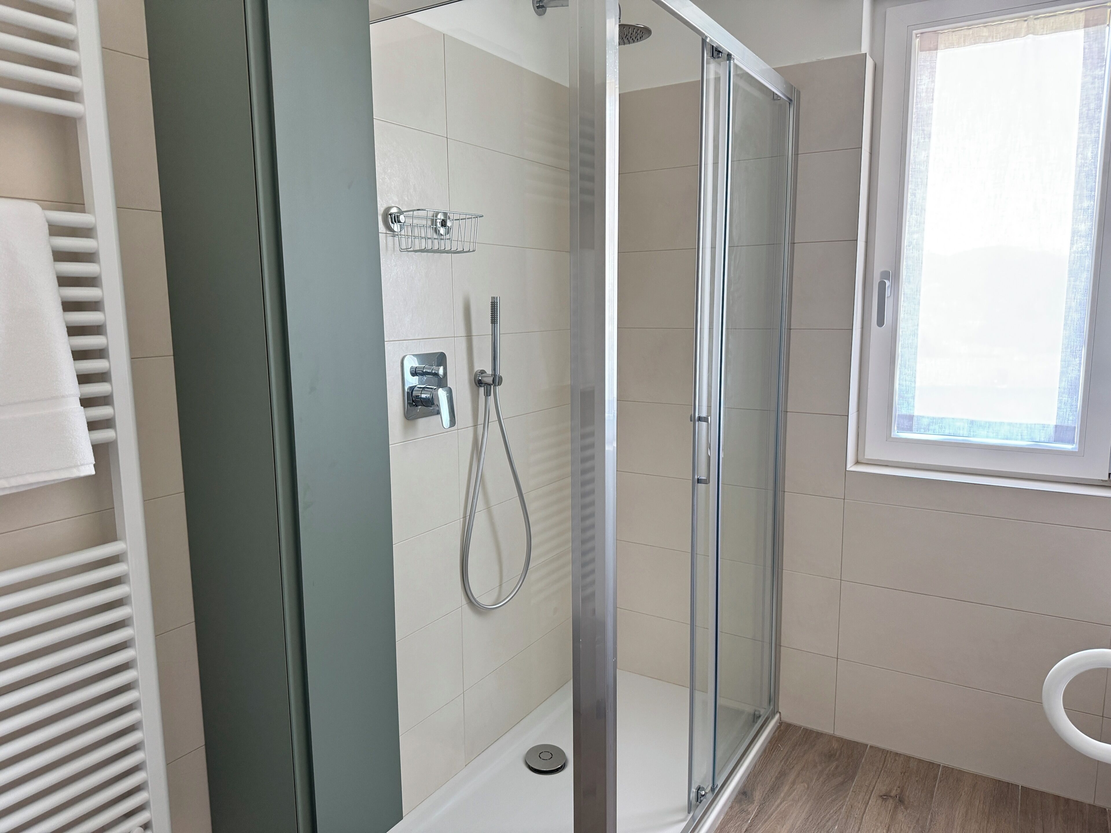 A modern bathroom with a glass-enclosed shower, a toilet, and a window.