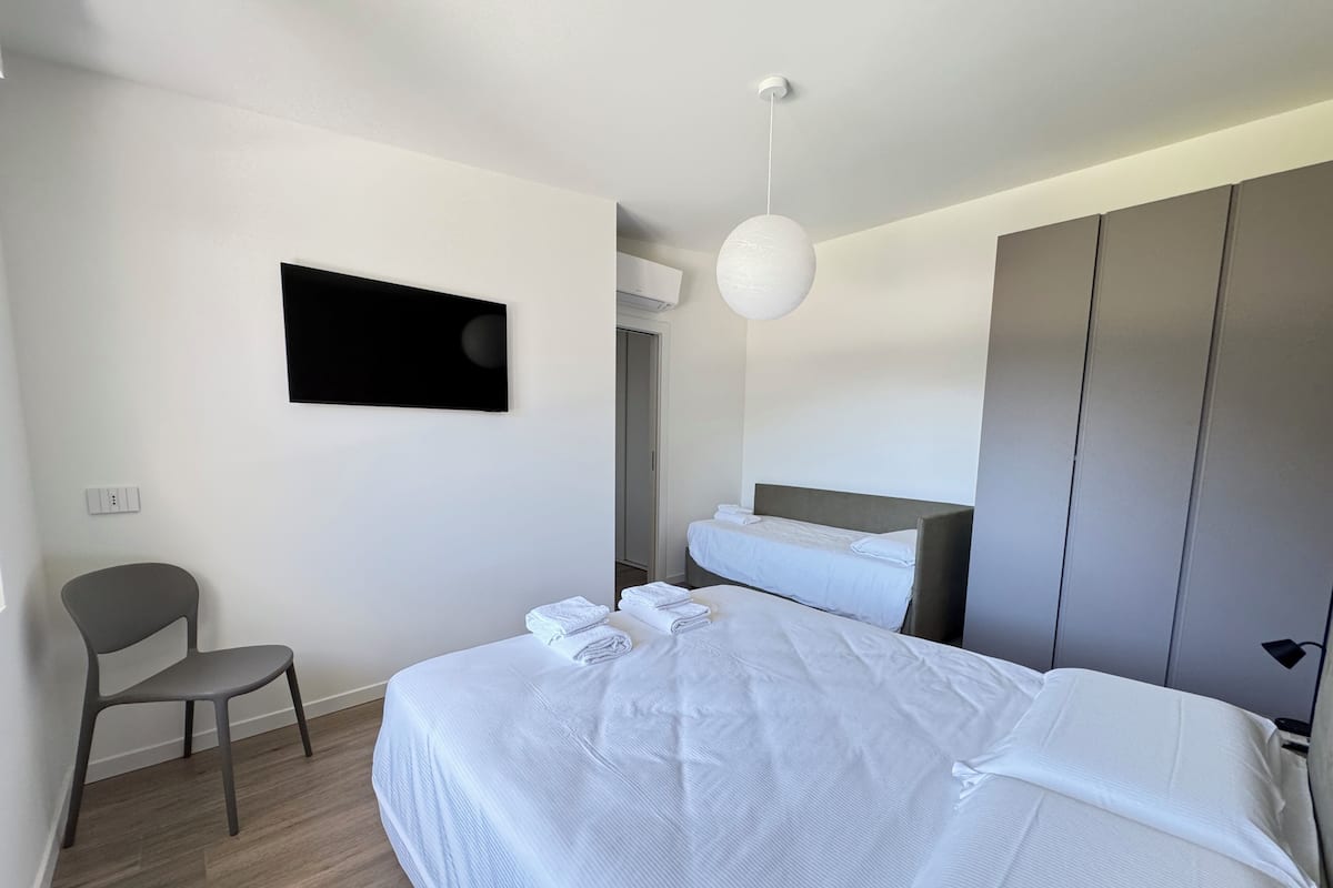 Une chambre d’hôtel moderne avec un grand lit, un téléviseur à écran plat fixé au mur, une chaise et une armoire.