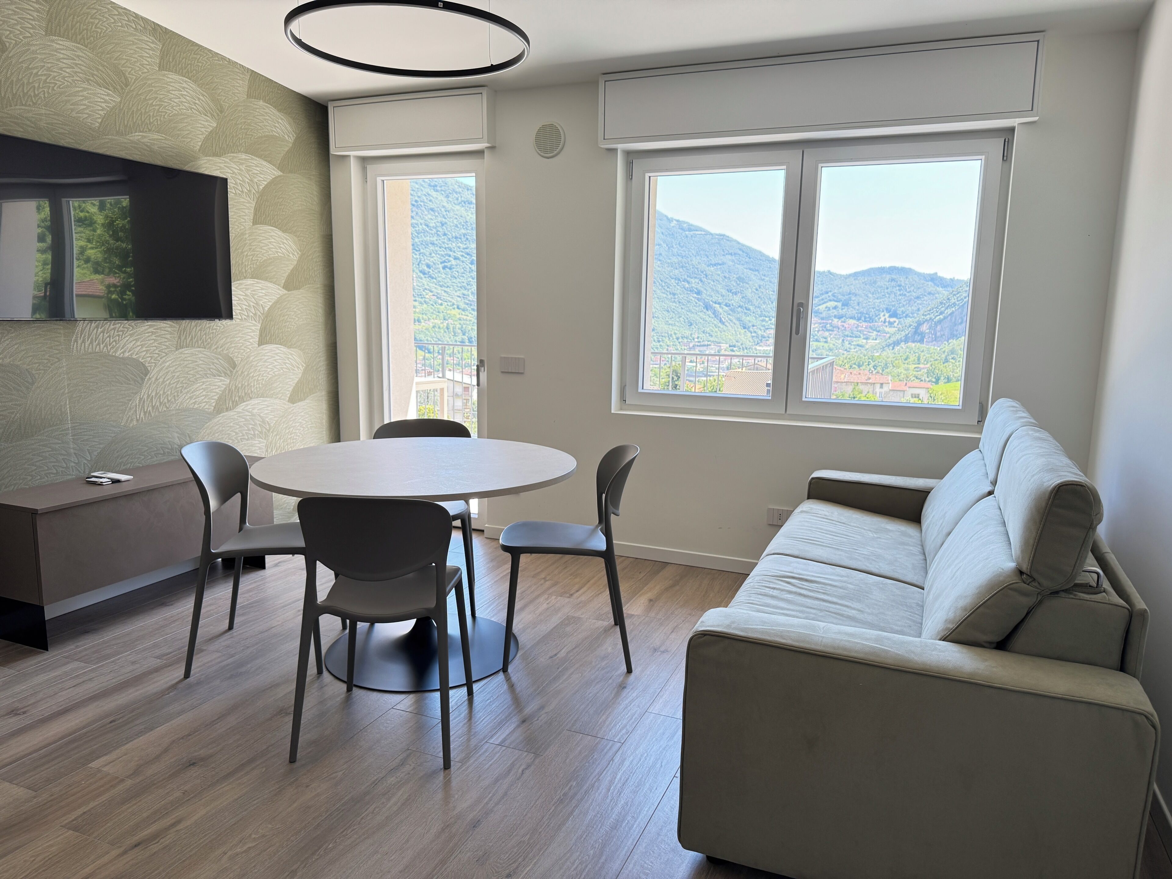 A modern living room with a round table, two chairs, a sofa, and a TV mounted on the wall.
