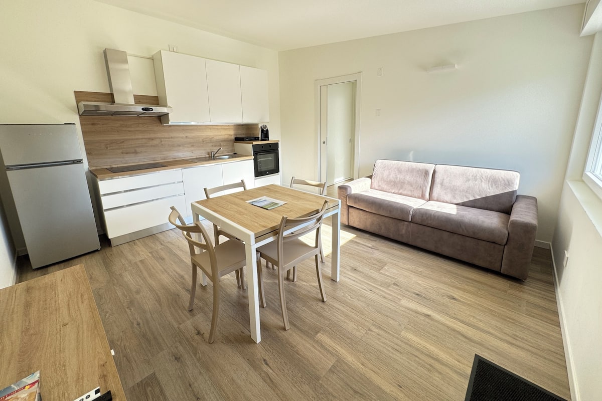 Un espace de vie compact comprenant un coin cuisine, un coin repas avec une table et des chaises en bois, et un canapé.