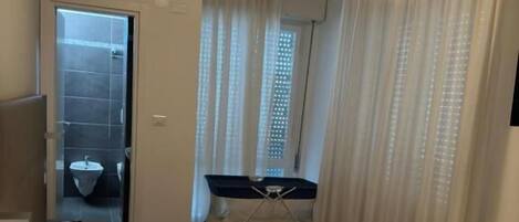 Habitación de hotel con cama, teléfono en la mesita de noche, escritorio con silla y ventana con cortinas.