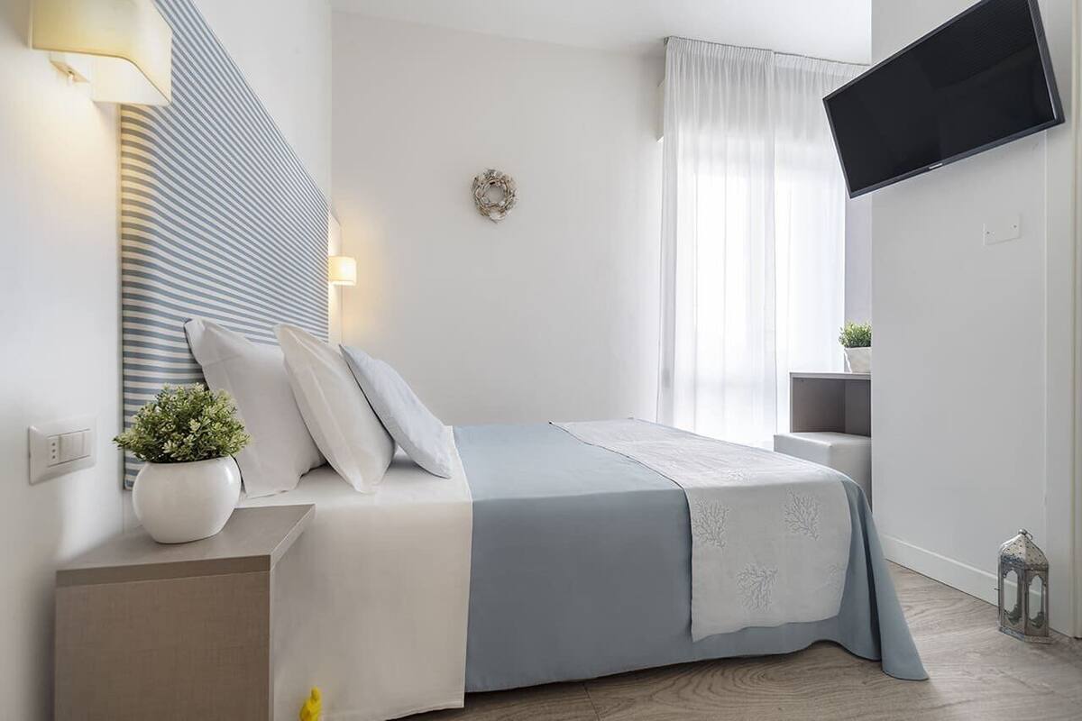 Ein modernes Schlafzimmer mit Bett, Nachttisch, Lampe und einem an der Wand montierten Flachbildfernseher.