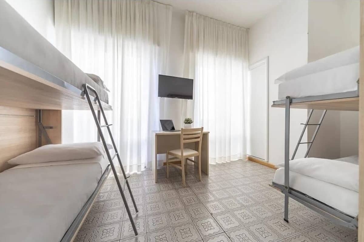 Ein kleines Hotelzimmer mit Etagenbetten, einem Schreibtisch, einem Stuhl und einem Fernseher.
