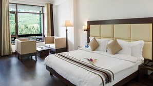 A hotel room with a large bed, two bedside tables, a desk, a chair, and a window with curtains. - The Tranquil Inn (Manali)