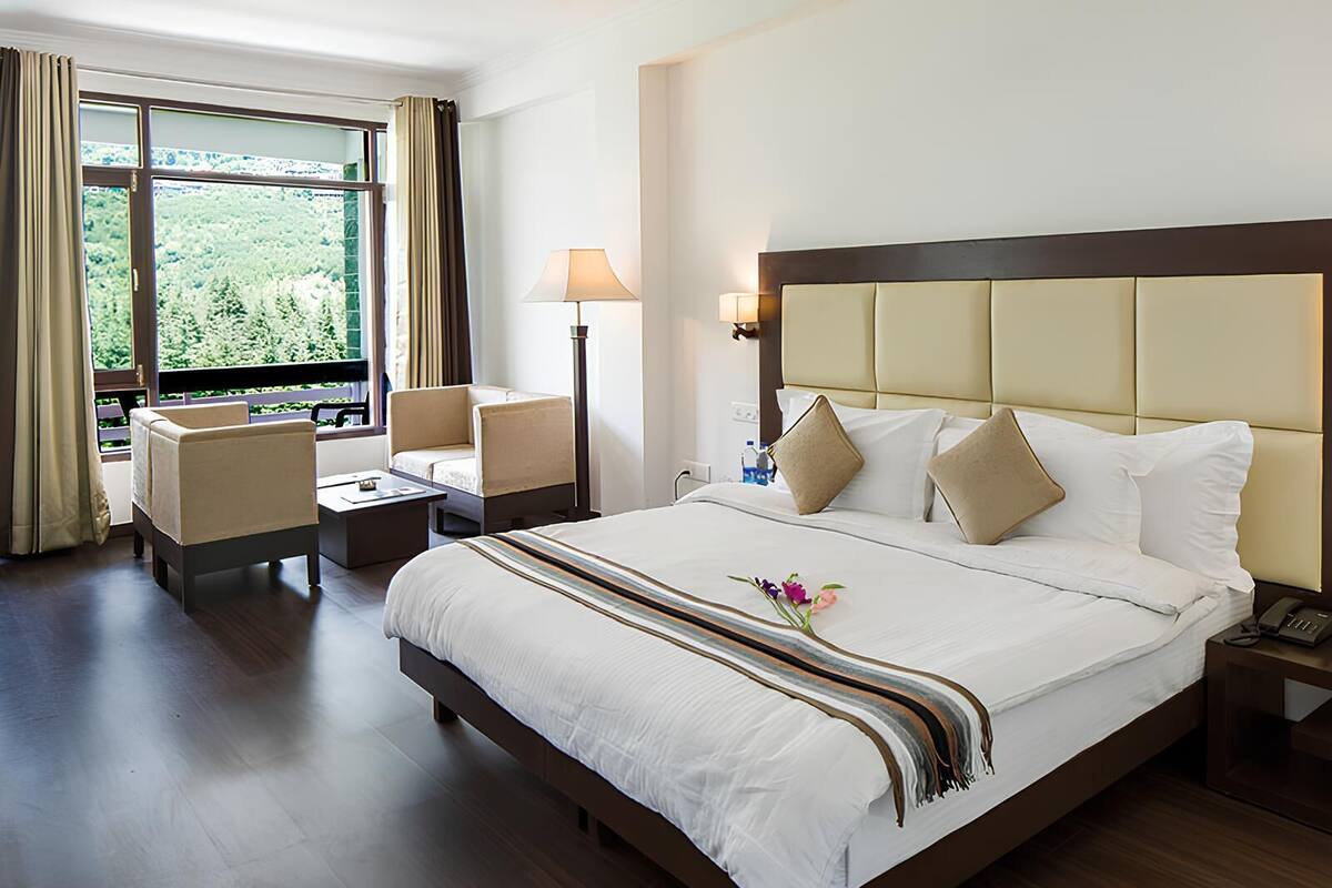 Une chambre d’hôtel avec un grand lit, deux tables de chevet, un bureau, une chaise et une fenêtre avec des rideaux.