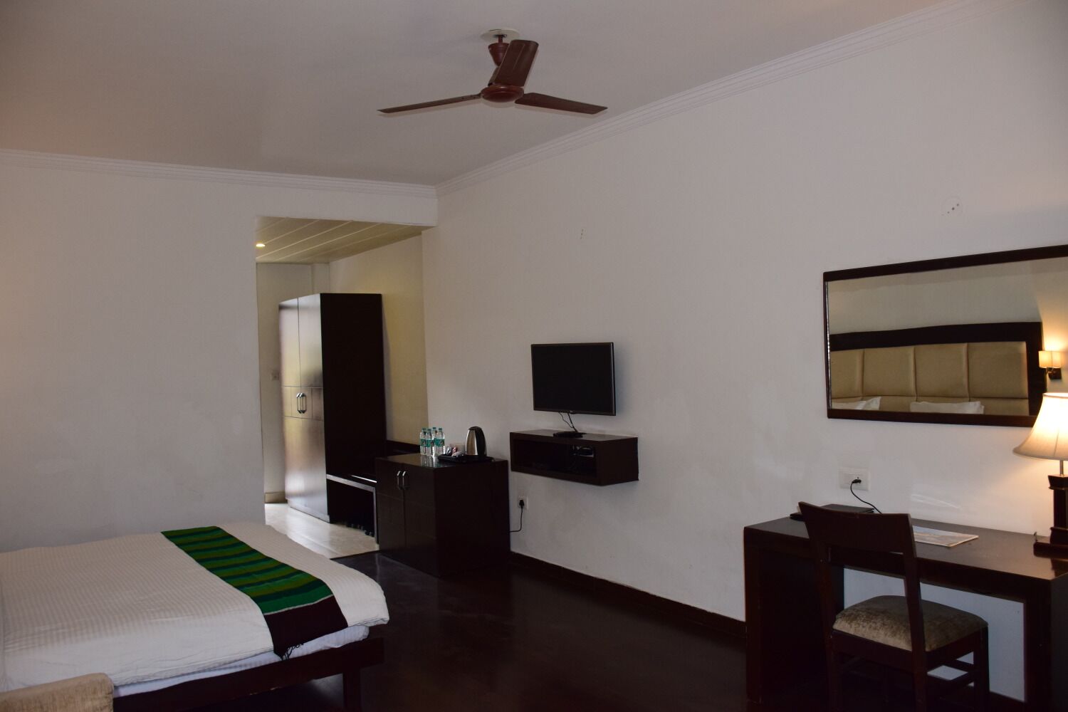 A hotel room with a bed, a desk, a television, a mirror, and a ceiling fan.