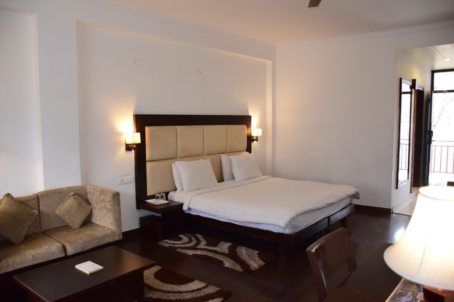 A hotel room with a bed, a sofa, a nightstand, and a lamp.