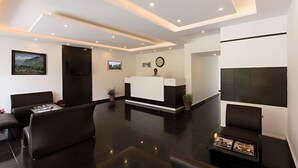 A modern hotel lobby with a reception desk, seating area, and a large window. - The Tranquil Inn (Manali)