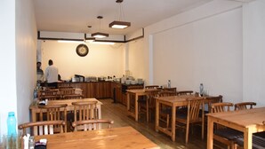 A restaurant with wooden tables and chairs, a counter with food items, and a clock on the wall. - The Tranquil Inn (Manali)