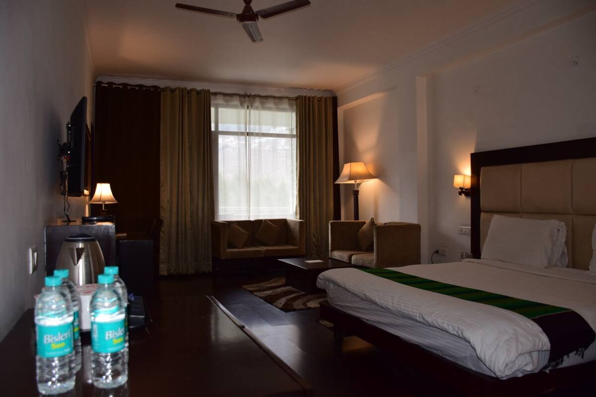 Une chambre d’hôtel comprenant un lit, deux fauteuils, un canapé, une télévision, une machine à café et trois bouteilles d’eau Bisleri.
