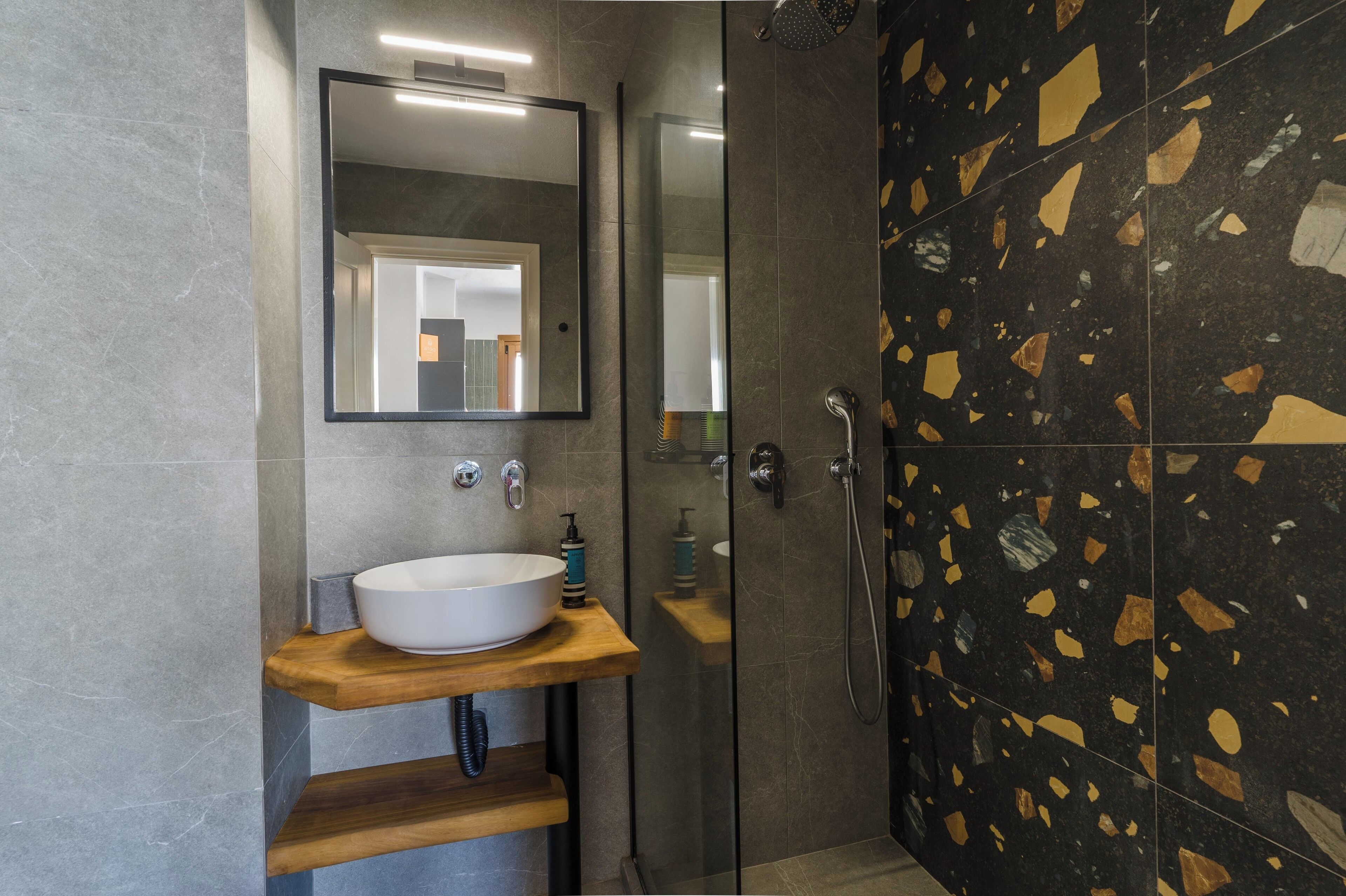 Une salle de bain moderne avec un grand miroir, un lavabo blanc et une douche aux carreaux noirs et dorés.
