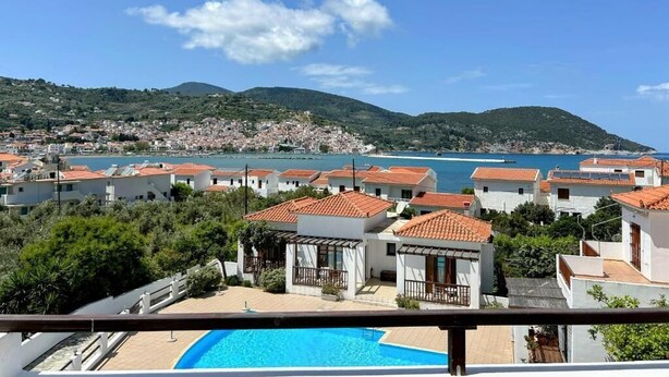 Vista costera con piscina, casas escalonadas y cielo azul despejado.
