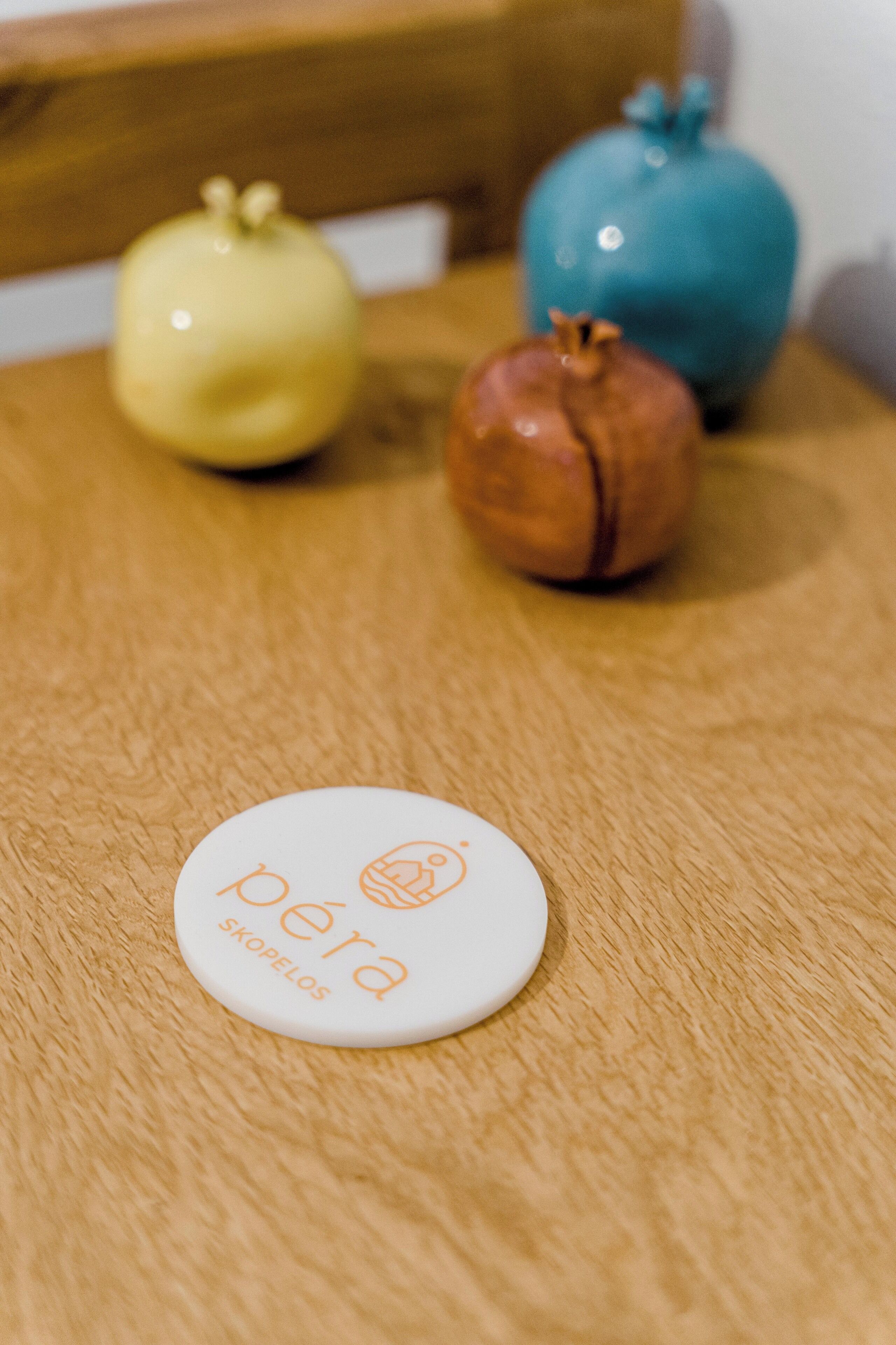Een houten tafel met een witte placemat waarop het logo ‘peira skopelos’ staat.