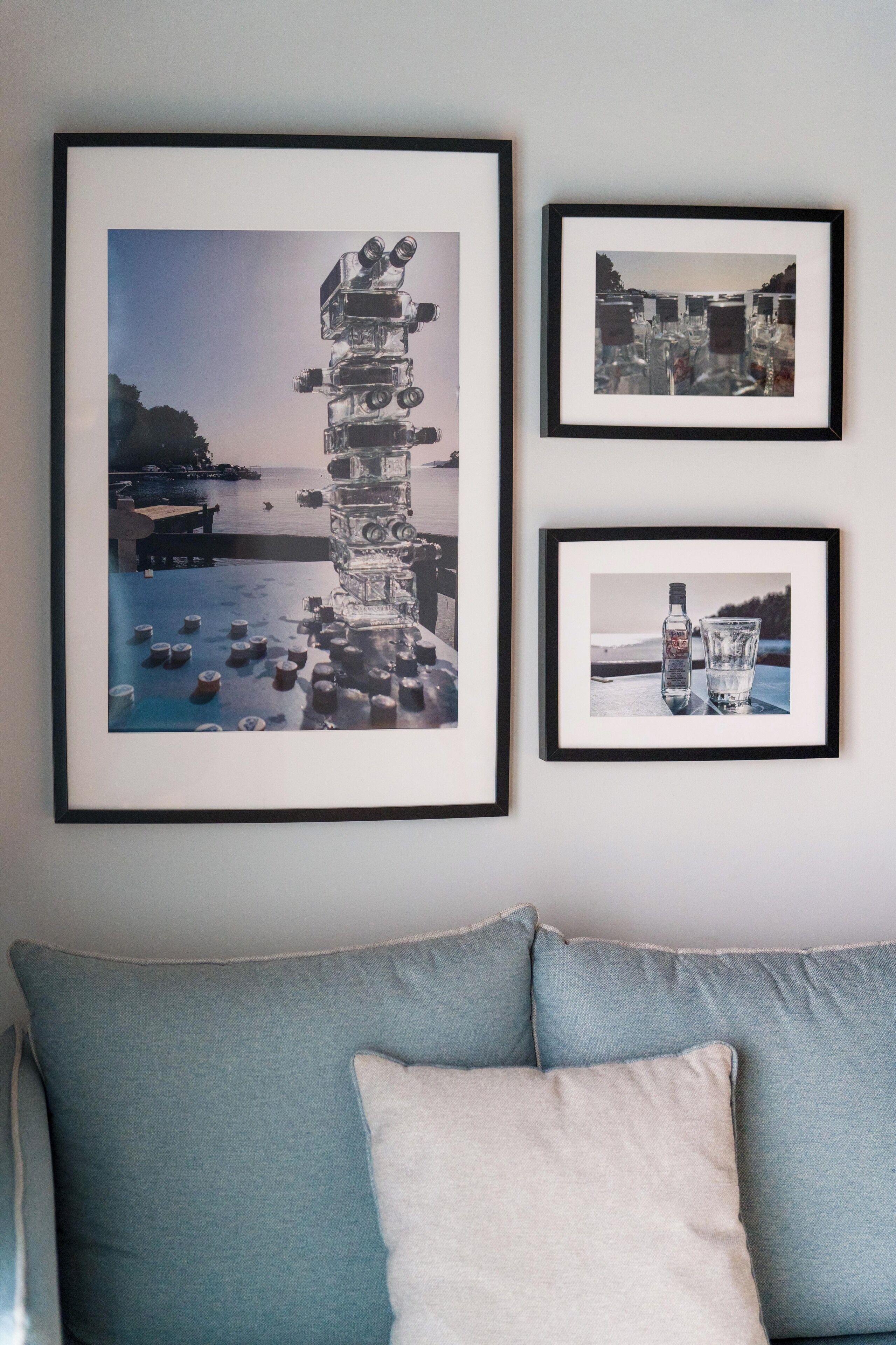 Een muur met drie ingelijste foto’s: één van een hoge stap objecten, één van een fles en glas, en één van een stadsgezicht.