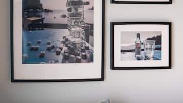 Een muur met drie ingelijste foto’s: één van een hoge stap objecten, één van een fles en glas, en één van een stadsgezicht.
