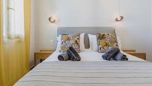 Una cama bien hecha con una colcha a rayas y dos almohadas con estampado floral. Hay dos mesitas de noche con lámparas a cada lado de la cama.
