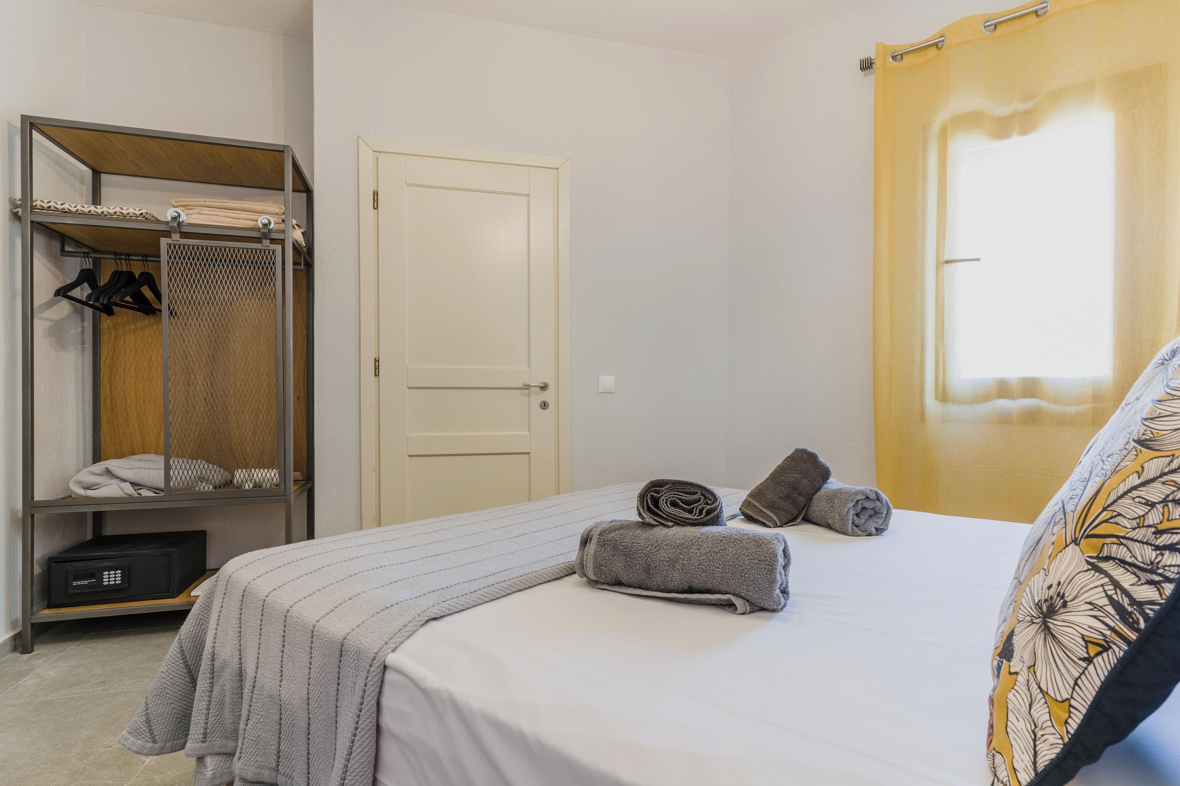 Un dormitorio con cama, armario, puerta y ventana con cortinas.