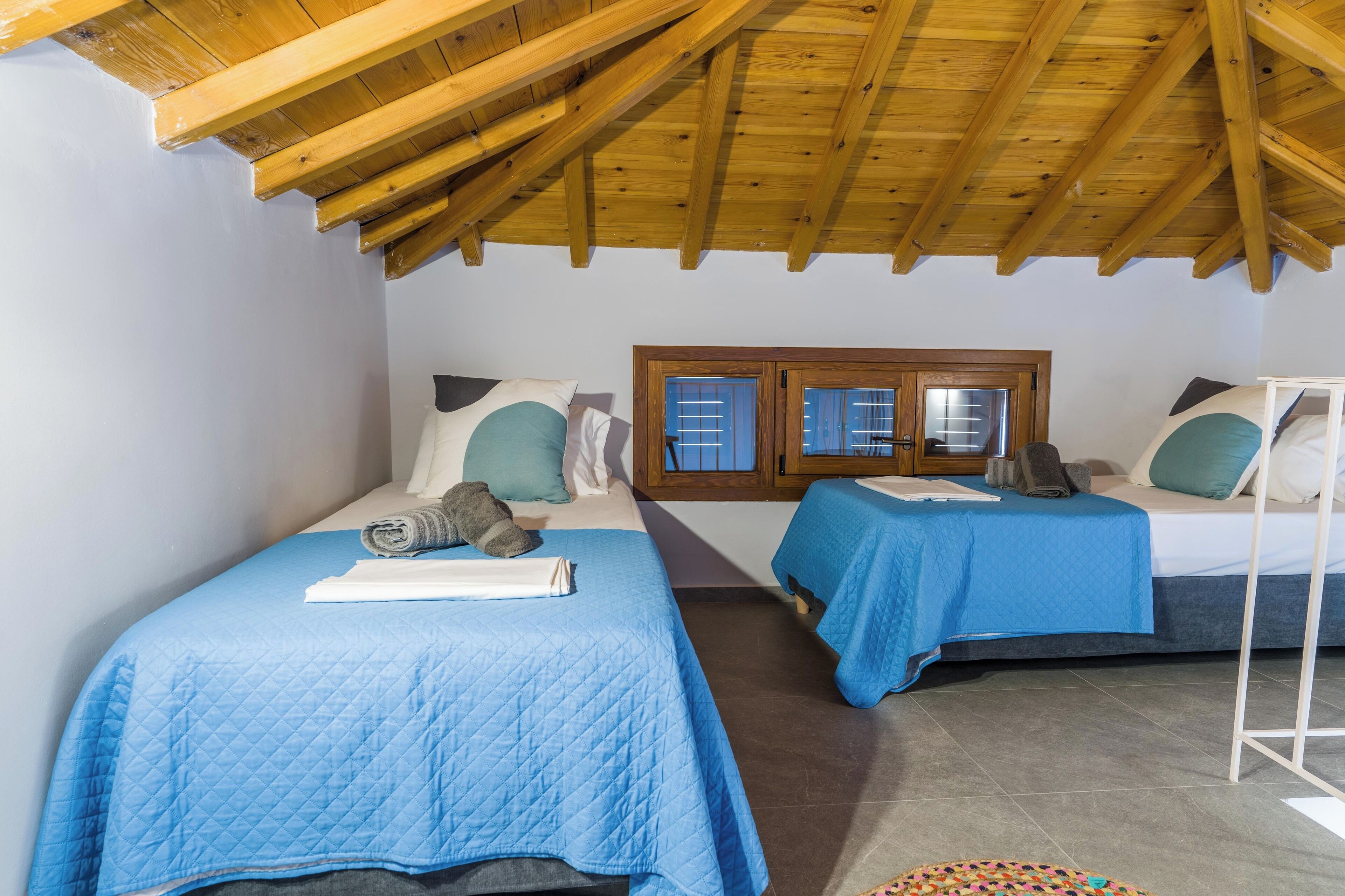 Un dormitorio con dos camas, vigas de madera en el techo, una ventana con vistas y una alfombra pequeña.