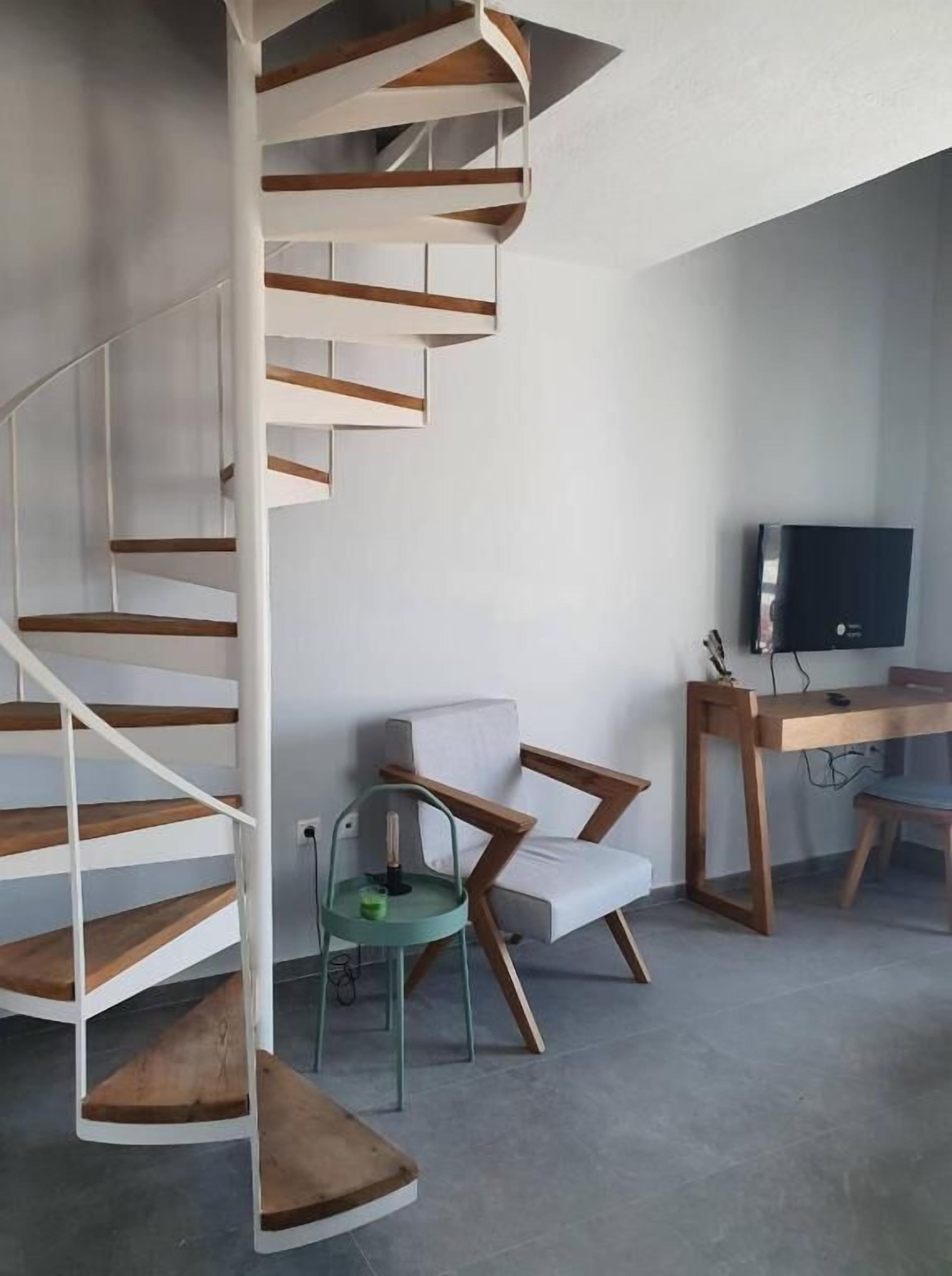 Un espace de vie moderne doté d’un escalier en colimaçon, d’un coin salon avec un canapé et des fauteuils, ainsi que d’un bureau équipé d’un ordinateur et d’une télévision.
