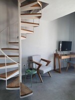 Un espacio de estar moderno con una escalera de caracol, una zona de descanso con sofá y sillones, y un escritorio con ordenador y televisor.