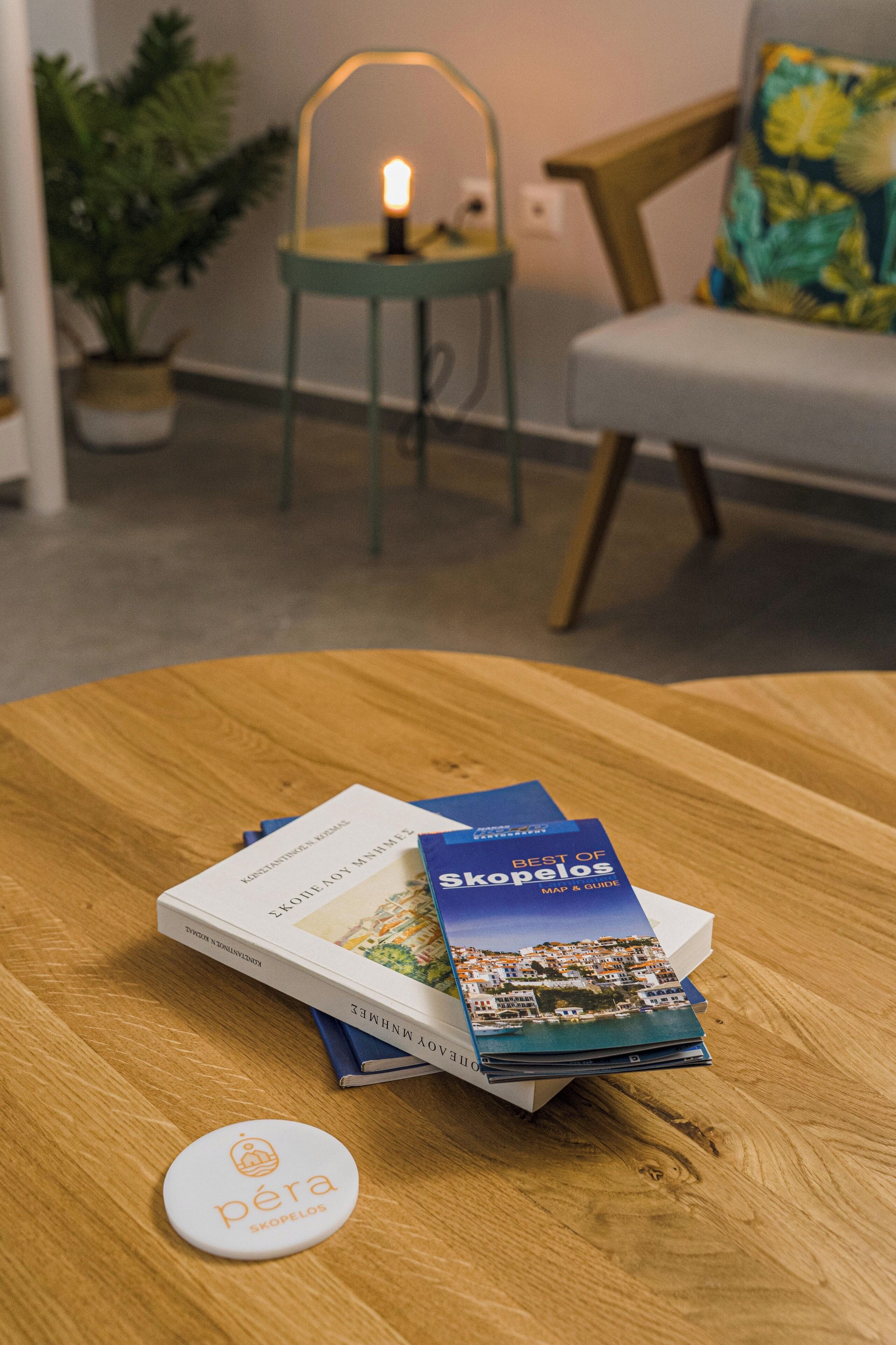 A wooden table with a book titled "Best of Skopelos" and a small white badge with the logo "pera Skopelos".