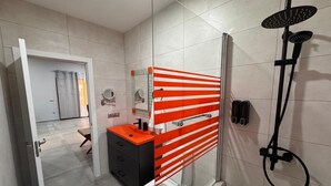 A modern bathroom with a glass shower enclosure, a white toilet, and a vanity with a red-striped towel rack.