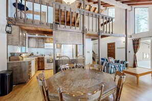 Un intérieur spacieux de style « loft », avec un plafond haut, des poutres apparentes, une grande table à manger et un coin salon confortable.
