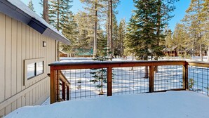 Una cabaña de madera con un porche cubierto de nieve y vistas a altos pinos.