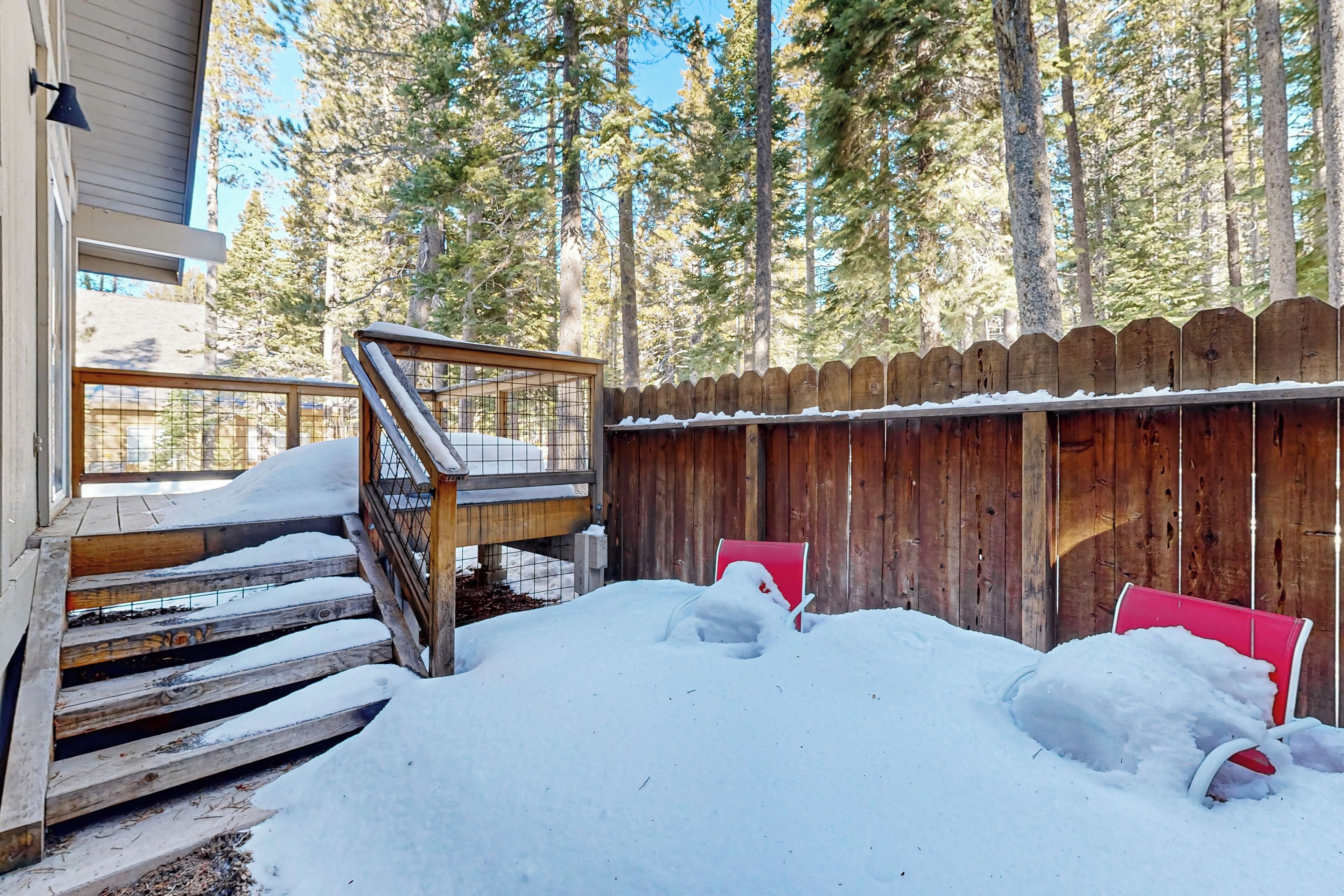 A wooden staircase leading to a deck, surrounded by a wooden fence and snow-covered ground.