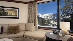 Een hotelkamer met een bank, een kleintje tafeltje en uitzicht op besneeuwde bergen door een groot raam.