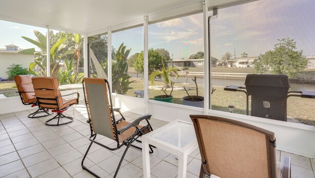 A sunlit patio with three chairs and a table, large windows offering a view of the surrounding area. - Waterfront Gulf Access Beach House w Lainai (Port Charlotte)