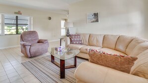 A living room with a beige sofa, a pink armchair, a glass coffee table, and a patterned rug. - Waterfront Gulf Access Beach House w Lainai (Port Charlotte)