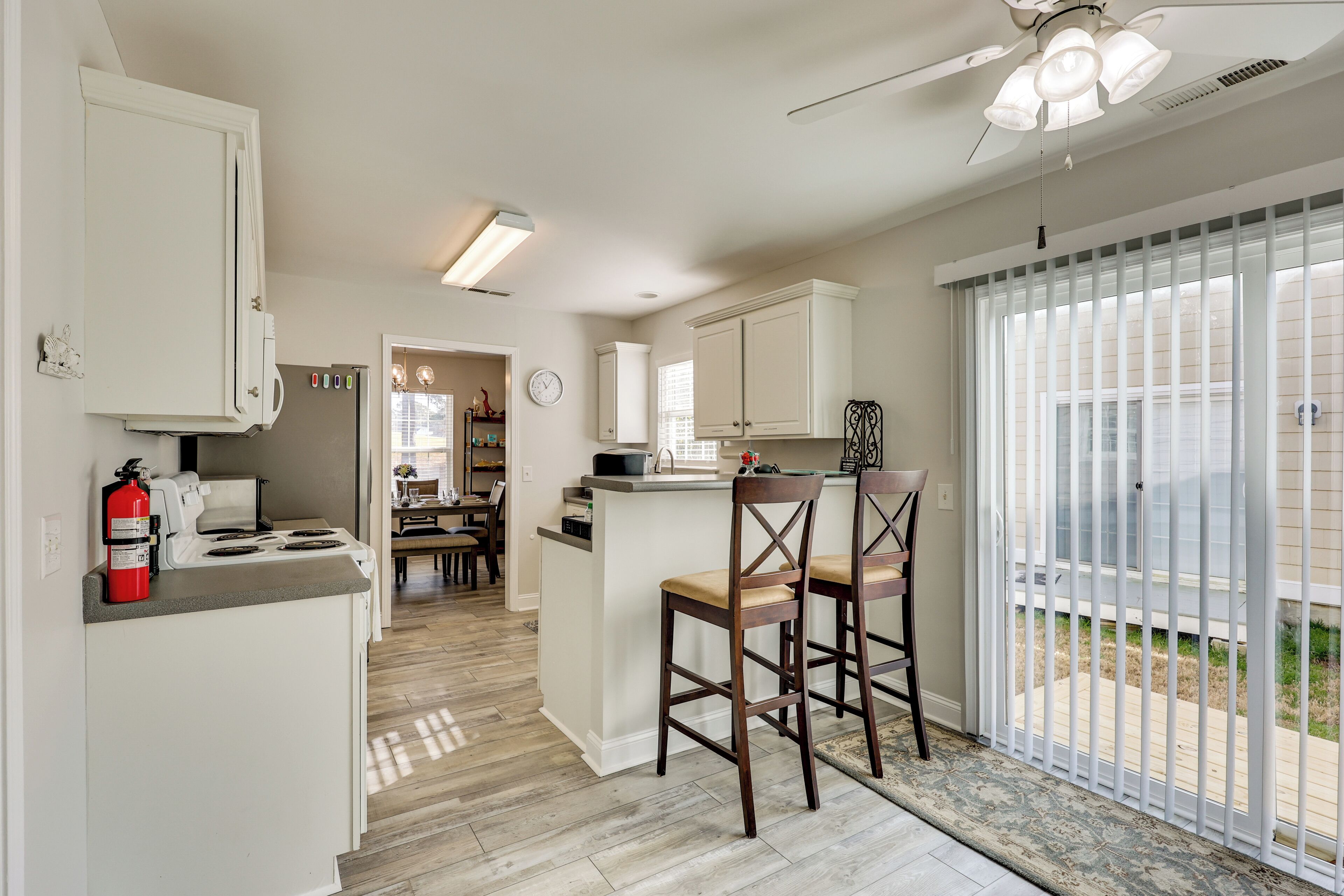 A kitchen with white cabinets, a stove, and a fire extinguisher. There are two wooden chairs and a ceiling fan.